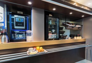 Eine moderne Frühstückstheke mit einer Kaffeemaschine, einem mit Lebensmitteln gefüllten Kühlschrank und einer Auswahl an Gebäck.
