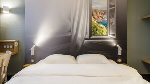 Een bed met uitzicht op een kustlandschap door een raam, een nachtkastje en een stoel.