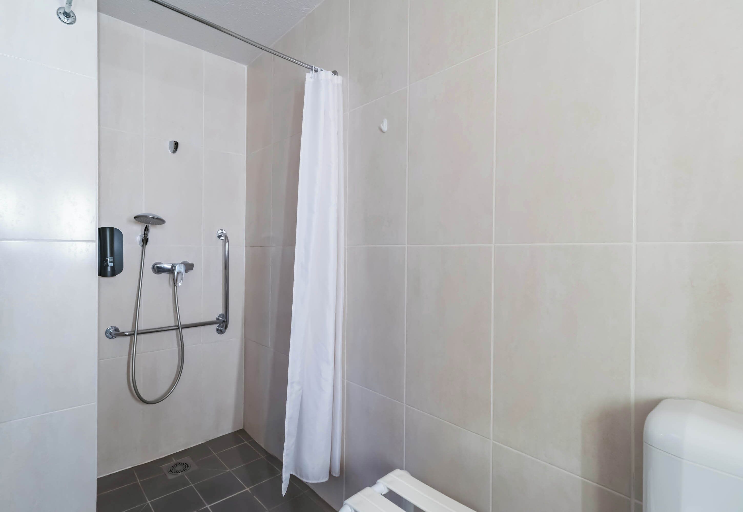 A shower area with a white curtain, a handheld showerhead, and a wall-mounted faucet.