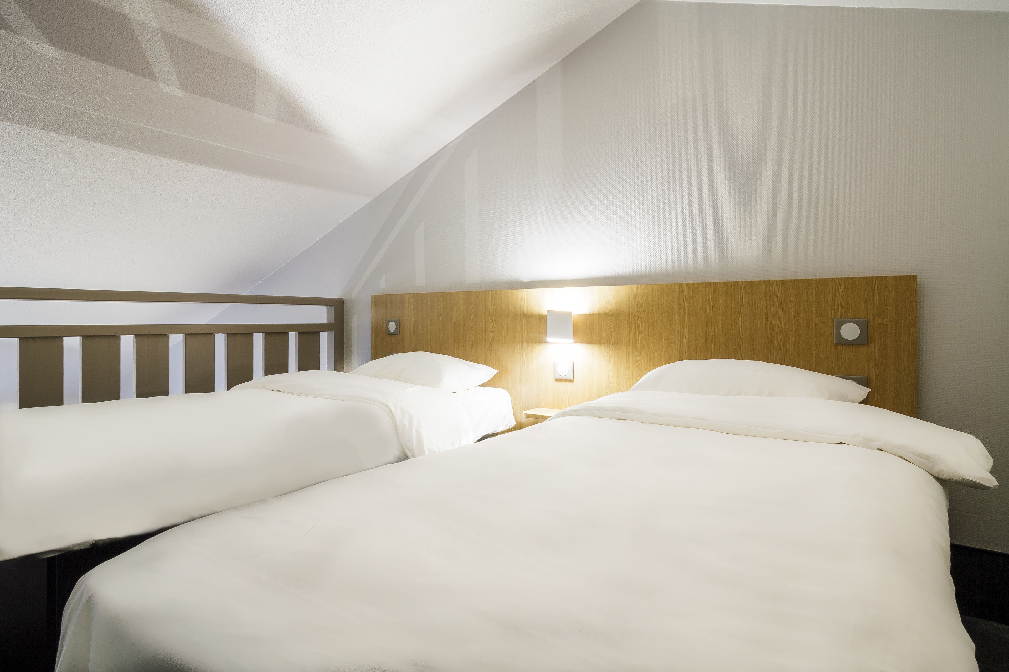 A hotel room with two single beds and a larger bed, all with white bedding.