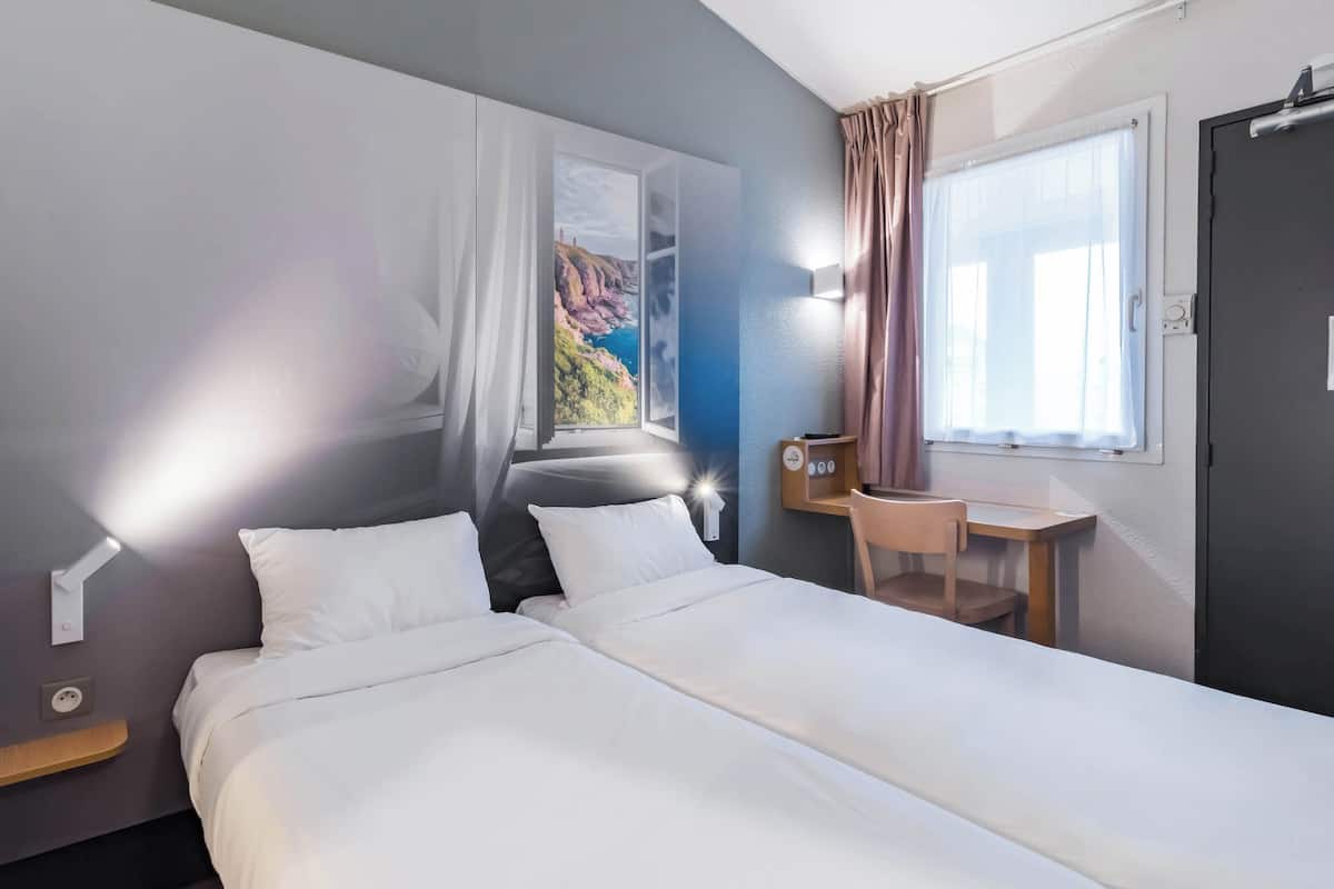 Une chambre d’hôtel avec un lit, un bureau, une chaise, une fenêtre donnant sur des falaises et un rideau.