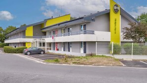 Ett hotell med en gul och vit fasad, en skylt som visar att det är ett bed and breakfast, och en parkeringsplats med en bil.