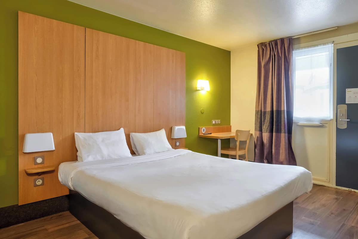 Ein Hotelzimmer mit einem großen Bett, einem Holzkopfteil, Nachttischlampen, einem kleinen Tisch und einem Sessel.