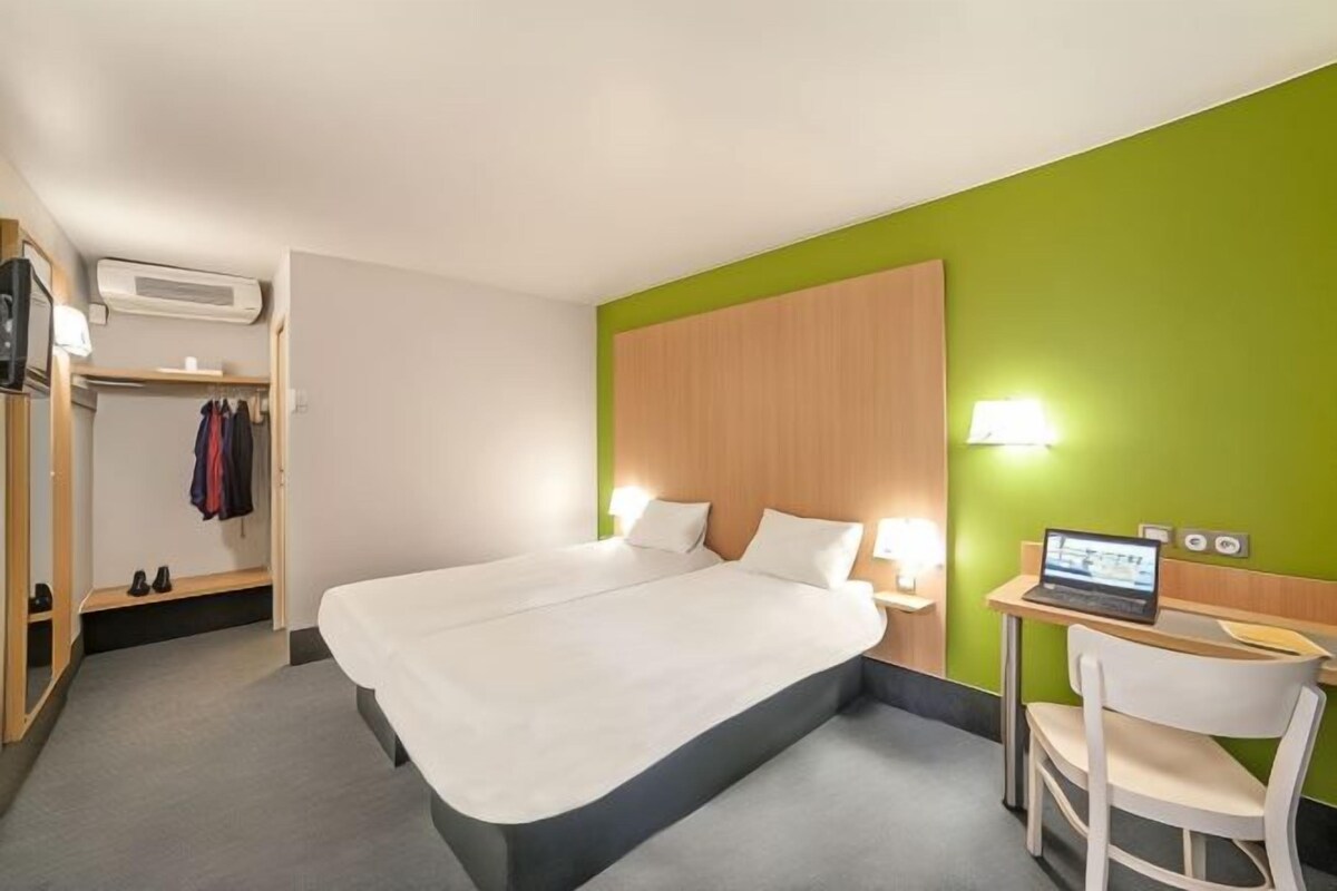 A hotel room with a bed, a desk with a laptop, a chair, a wardrobe, and a mirror.