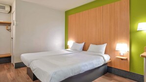 Ett hotellrum med en stor säng, en sänggavel i trä, två sänglampor och en vägg som är målad i en accentfärg – grönt.