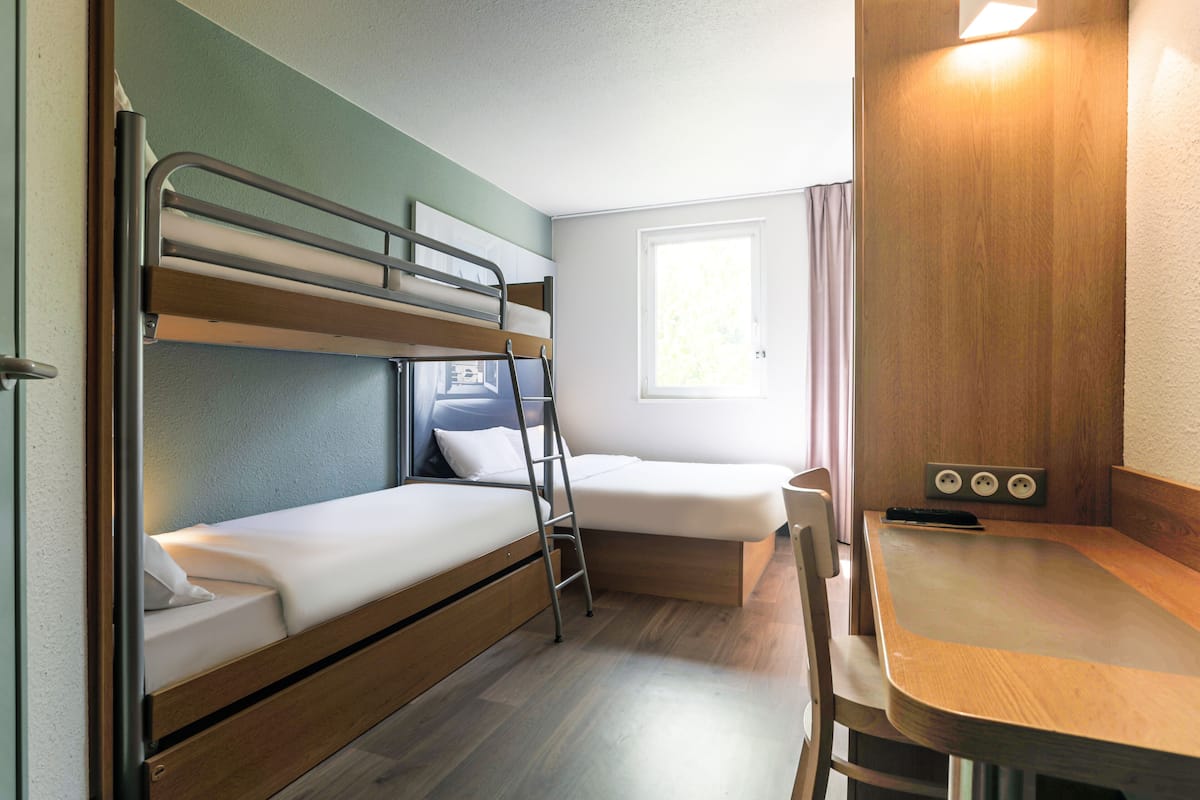 A bunk bed room with a desk and chair, a window, and a power outlet.