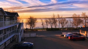 A building with a balcony overlooking a parking area and a body of water.