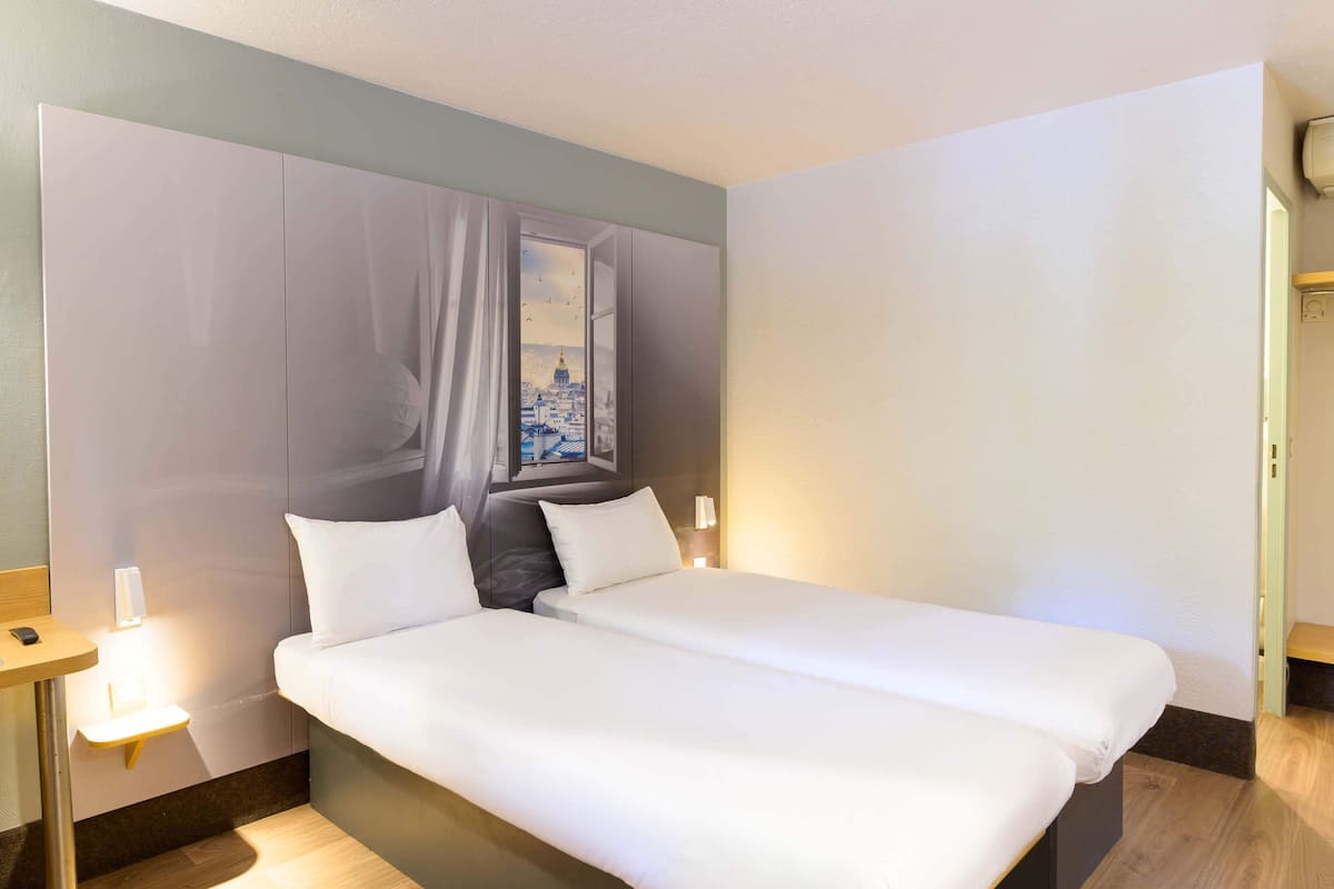 A double bed in a hotel room with a view of a cityscape through an open window.
