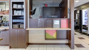 A reception area with a counter, shelves with plates and cups, a computer, and a phone. - B&B HOTEL Châlons-en-Champagne (Chalons-en-Champagne)