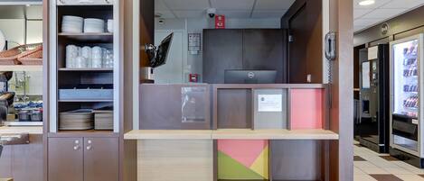 A reception area with a counter, shelves with plates and cups, a computer, and a phone.