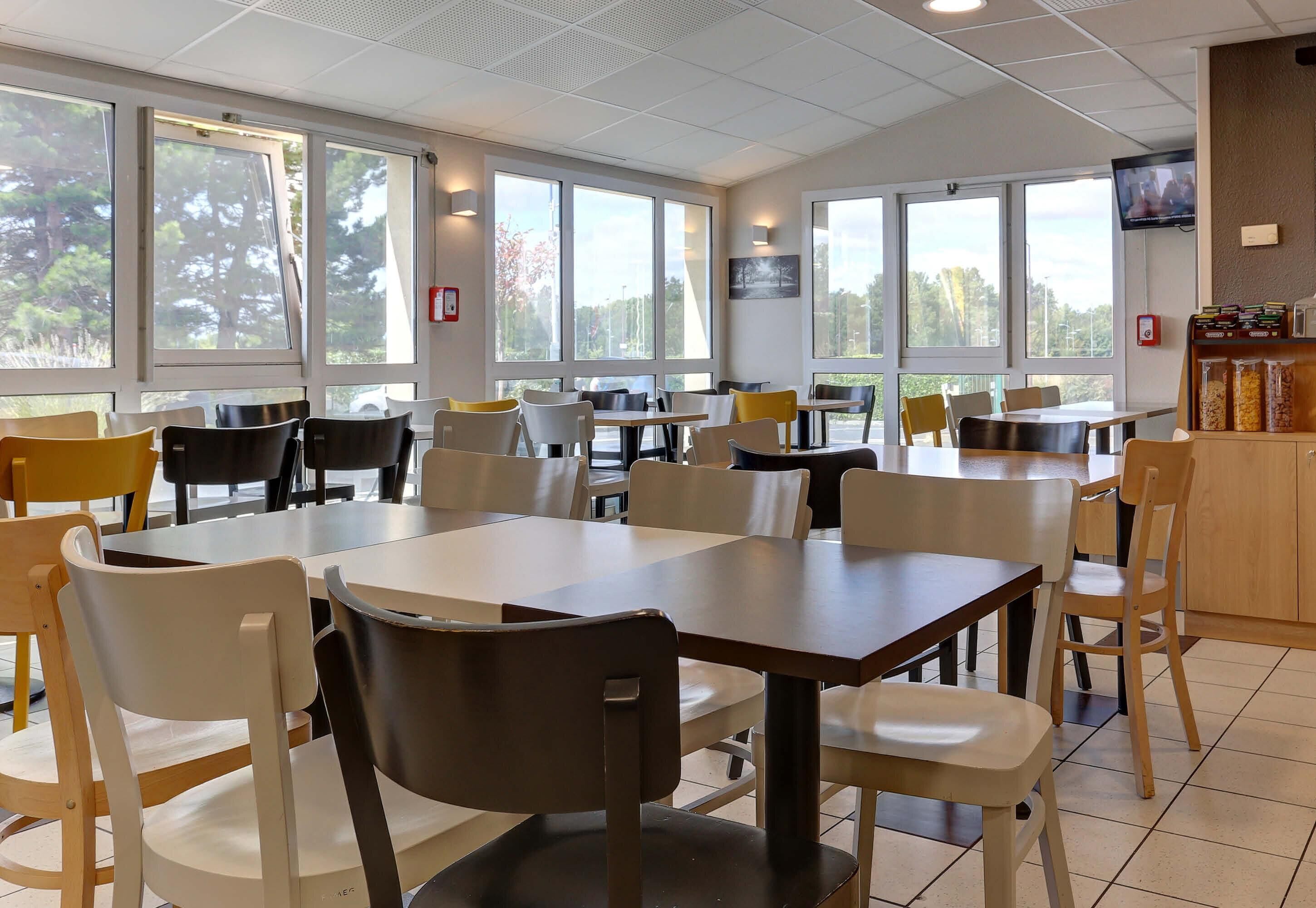 L’intérieur d’un restaurant, avec des tables et des chaises, de grandes fenêtres, un téléviseur et un extincteur.