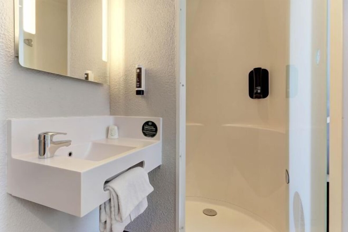Un baño moderno con un lavabo blanco, espejo y ducha con mampara de vidrio.
