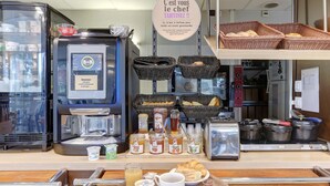 A bakery counter with a coffee machine, baskets of bread, jars of spreads, and a tray of pastries. - B&B HOTEL Châlons-en-Champagne (Chalons-en-Champagne)