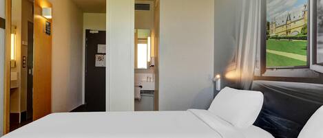 A hotel room with a bed, a bathroom, and a view of a building through a window.
