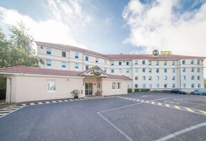 Un hotel tipo casa de huéspedes con estacionamiento y un edificio de múltiples ventanas.