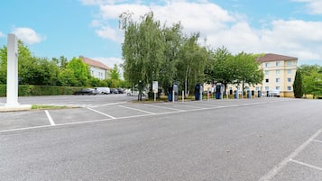 A parking lot with marked spaces, a white pillar, and a row of trees.