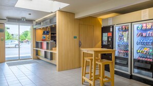 Een schoon, modern interieur met een houten toonbank, een kleine tafel met krukjes en automaten gevuld met drankjes en snacks.