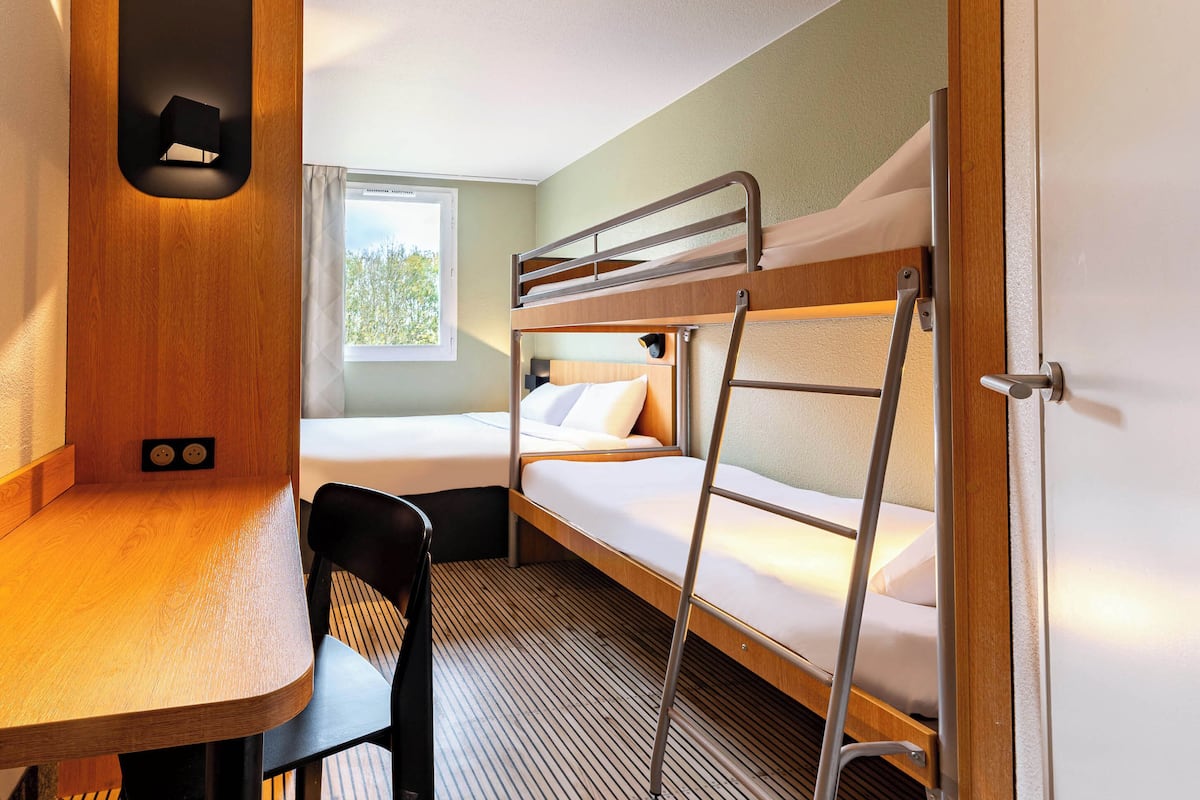 A compact hotel room with bunk beds, a wooden desk, and a window with a view.