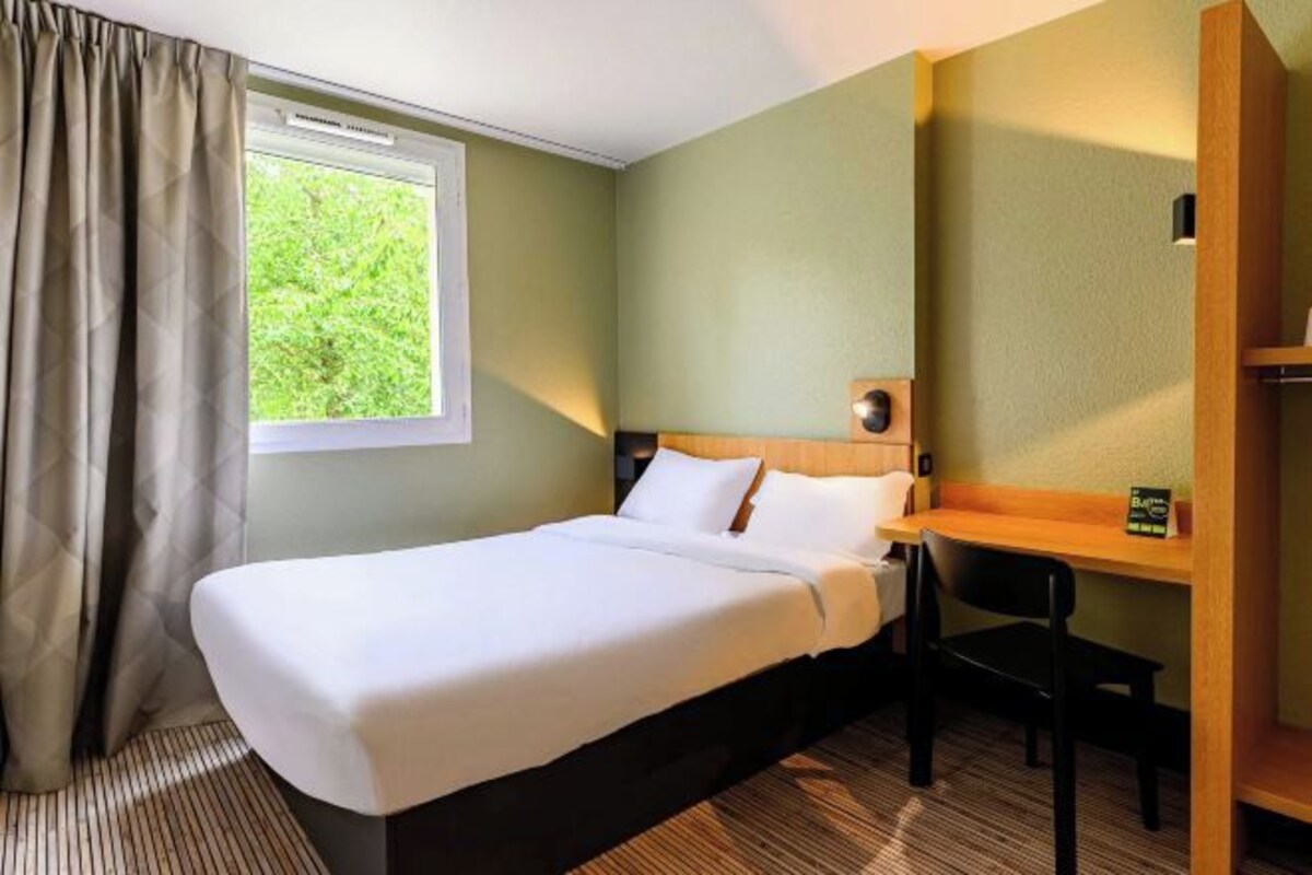 A hotel room with a bed, a desk, a chair, and a window with curtains.