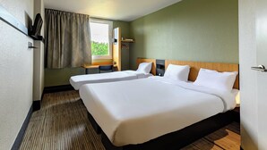 Hotelkamer met twee bedden, een bureau, een stoel, een raam met gordijnen en uitzicht op groen.