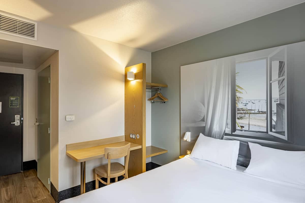 Ein Hotelzimmer mit Bett, Schreibtisch, Stuhl, Spiegel, Fenster und Tür.