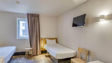 Hotelkamer met twee eenpersoonsbedden, een tafeltje, een stoel, een aan de muur bevestigde televisie en een raam met gordijnen.