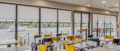Un restaurante con mesas y sillas, ventanas amplias y vista a un estacionamiento.