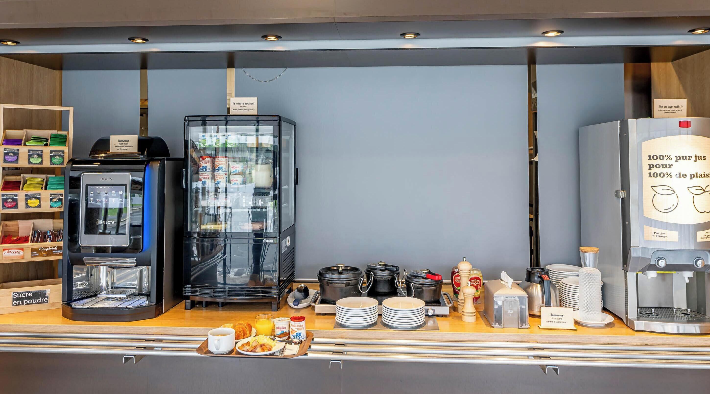Ein Frühstücksbuffet mit einer Kaffeemaschine, einem Kühlschrank und einer Auswahl an Speisen.