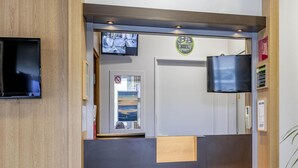 Un espace d’accueil avec un comptoir de réception en bois, un téléviseur fixé au mur et un tableau représentant une plage.