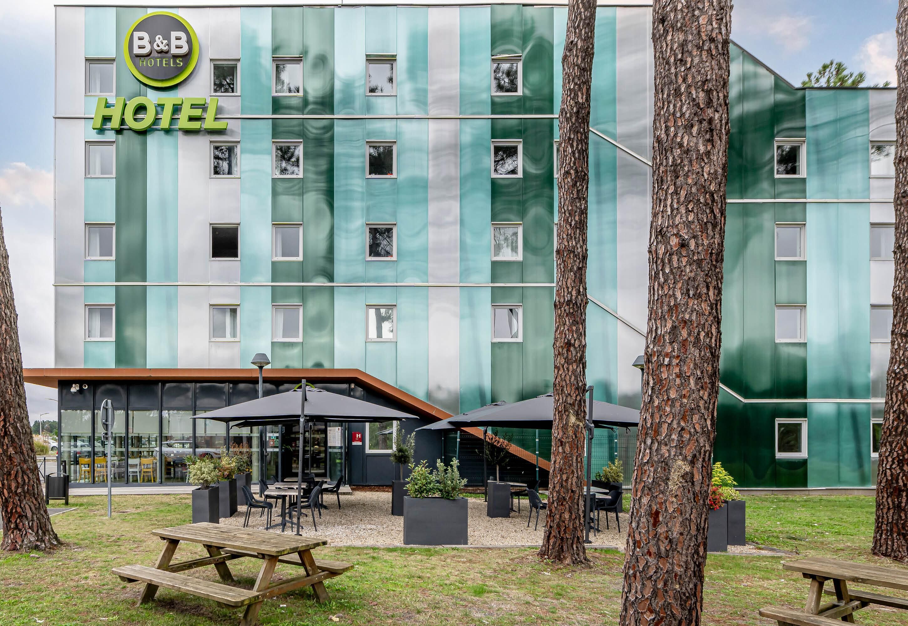 Un hôtel-restaurant de type « bed and breakfast » doté d’une façade moderne, d’un espace extérieur aménagé avec des sièges et d’un coin pique-nique.