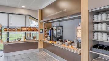 Un café moderne avec un comptoir où sont exposées des pâtisseries et du matériel pour préparer le café.