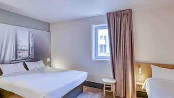 Ein Hotelzimmer mit einem Bett, einem kleinen Hocker, einem Fenster mit Vorhängen und Blick nach draußen.