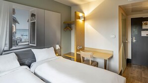 Une chambre d’hôtel avec deux lits, un bureau, une chaise, une fenêtre avec des rideaux et une vue sur la mer.