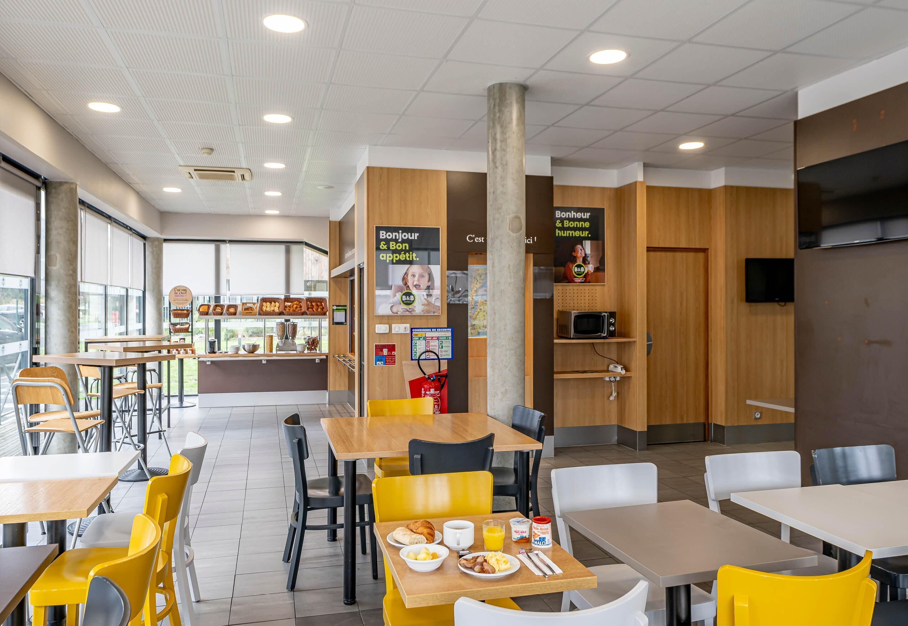 Ein modernes Café mit Holztischen und -stühlen, einer sichtbaren Speisekarte und einer Küchenzeile.