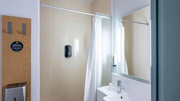 A bathroom with a shower, a hand dryer, a towel dispenser, and a mirror.