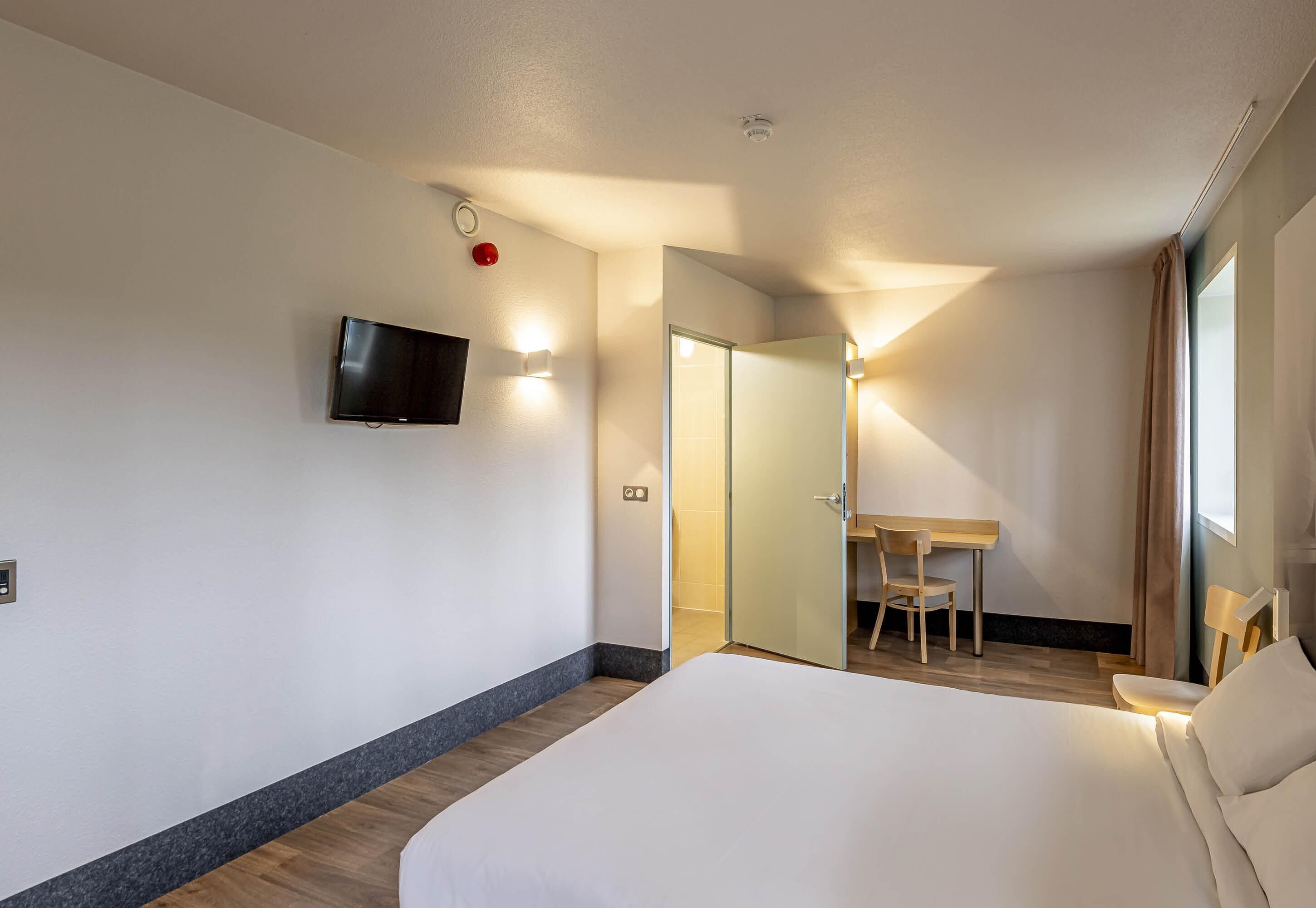 A hotel room with a bed, a desk, a chair, a TV, and a sliding door.