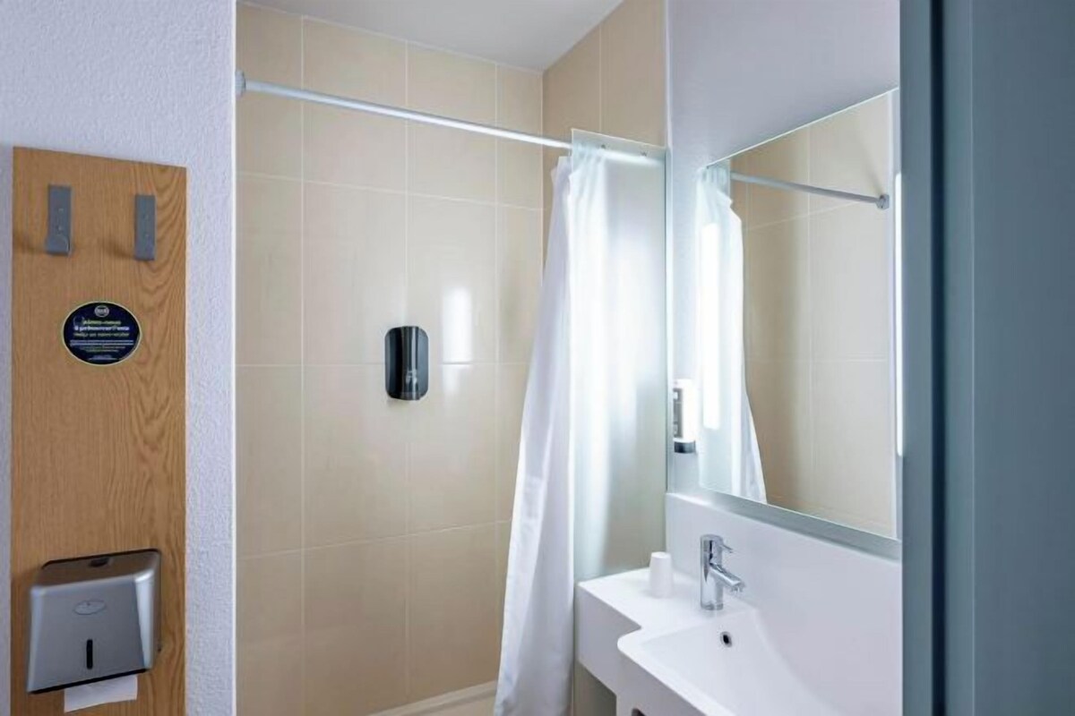 A modern bathroom with a shower, a hand dryer, and a mirror.