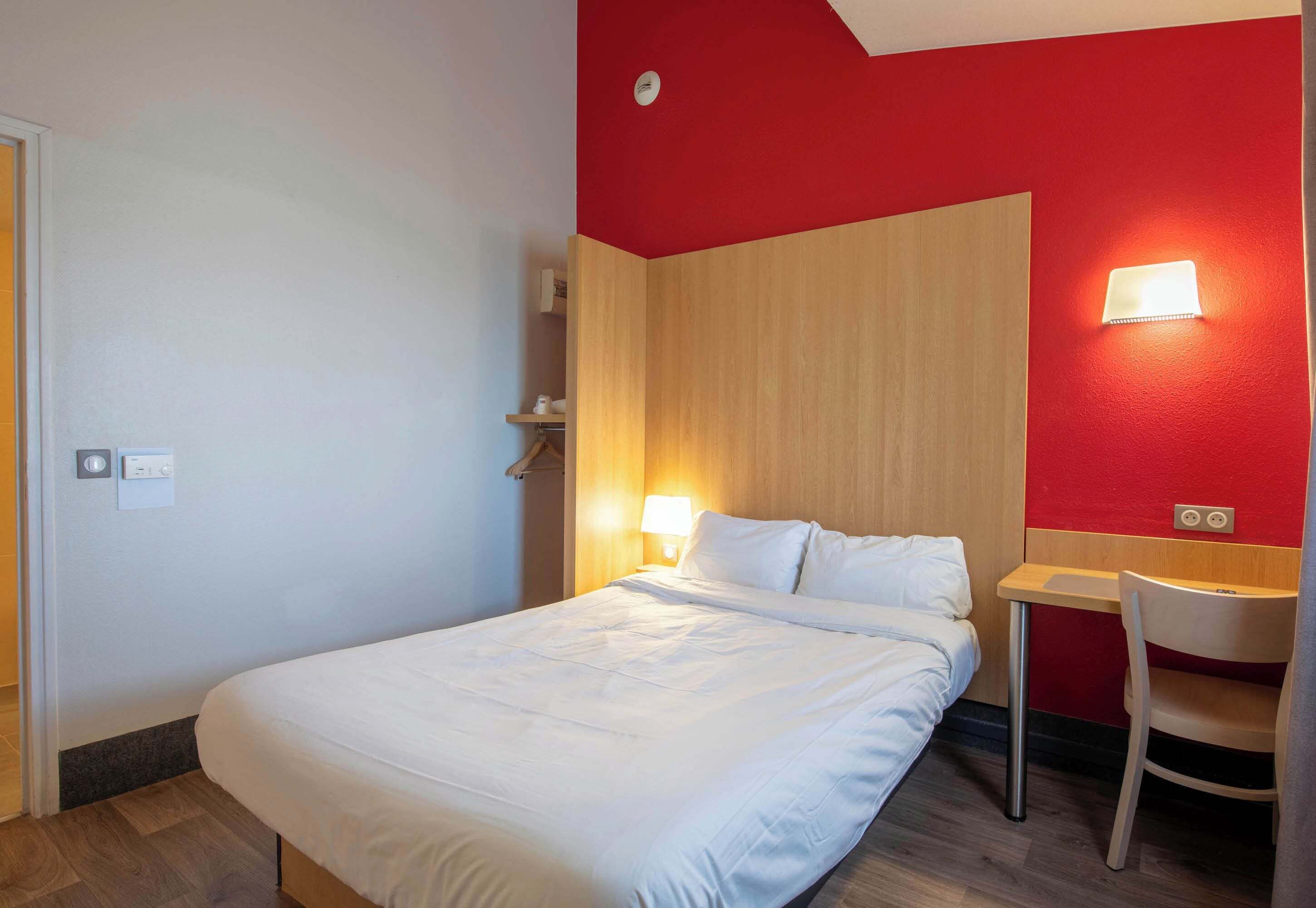 A hotel room with a bed, bedside table, chair, and wall-mounted light fixtures.