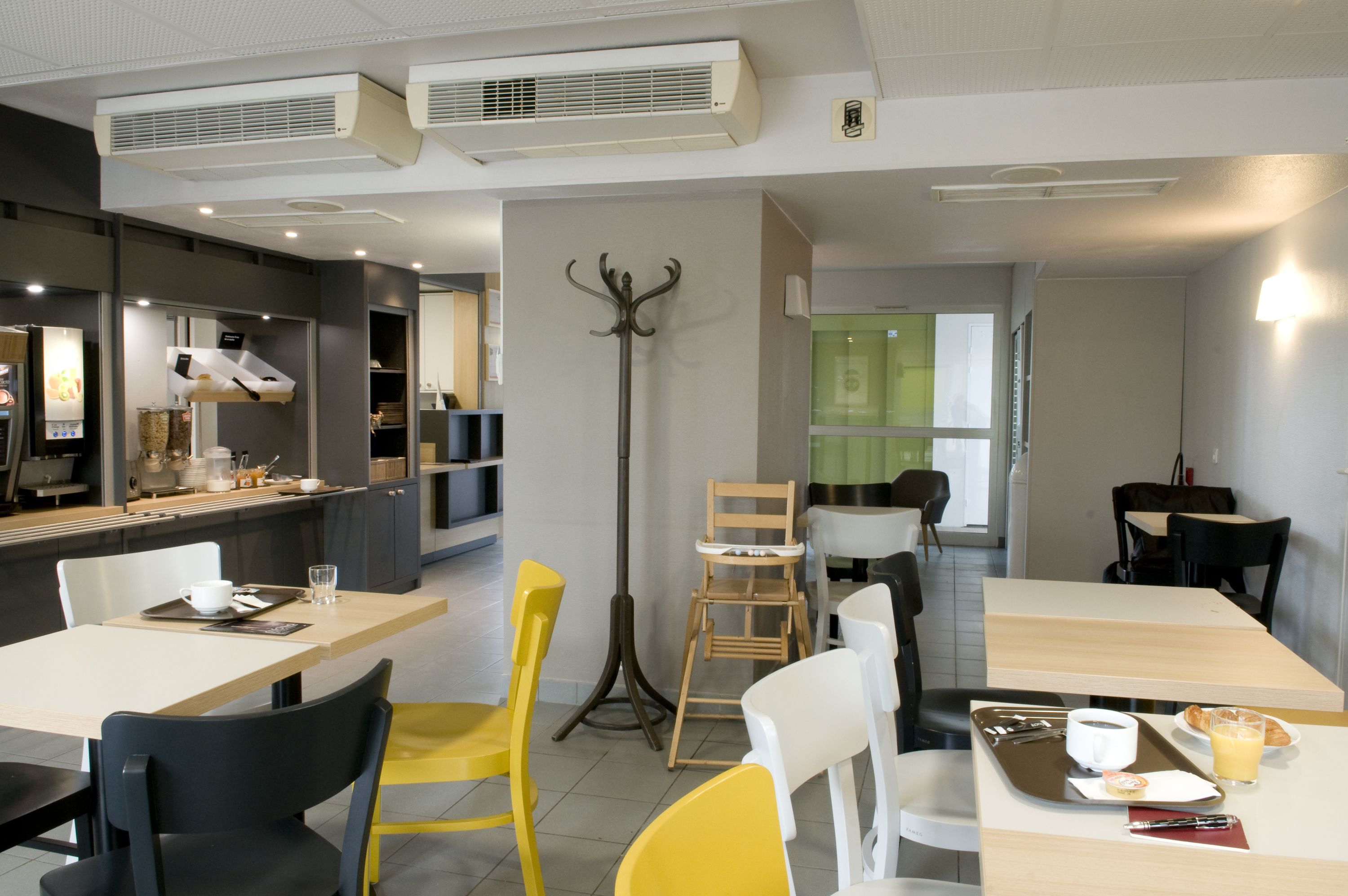 A modern cafe with tables and chairs, a counter with a menu, and a decorative wall piece.