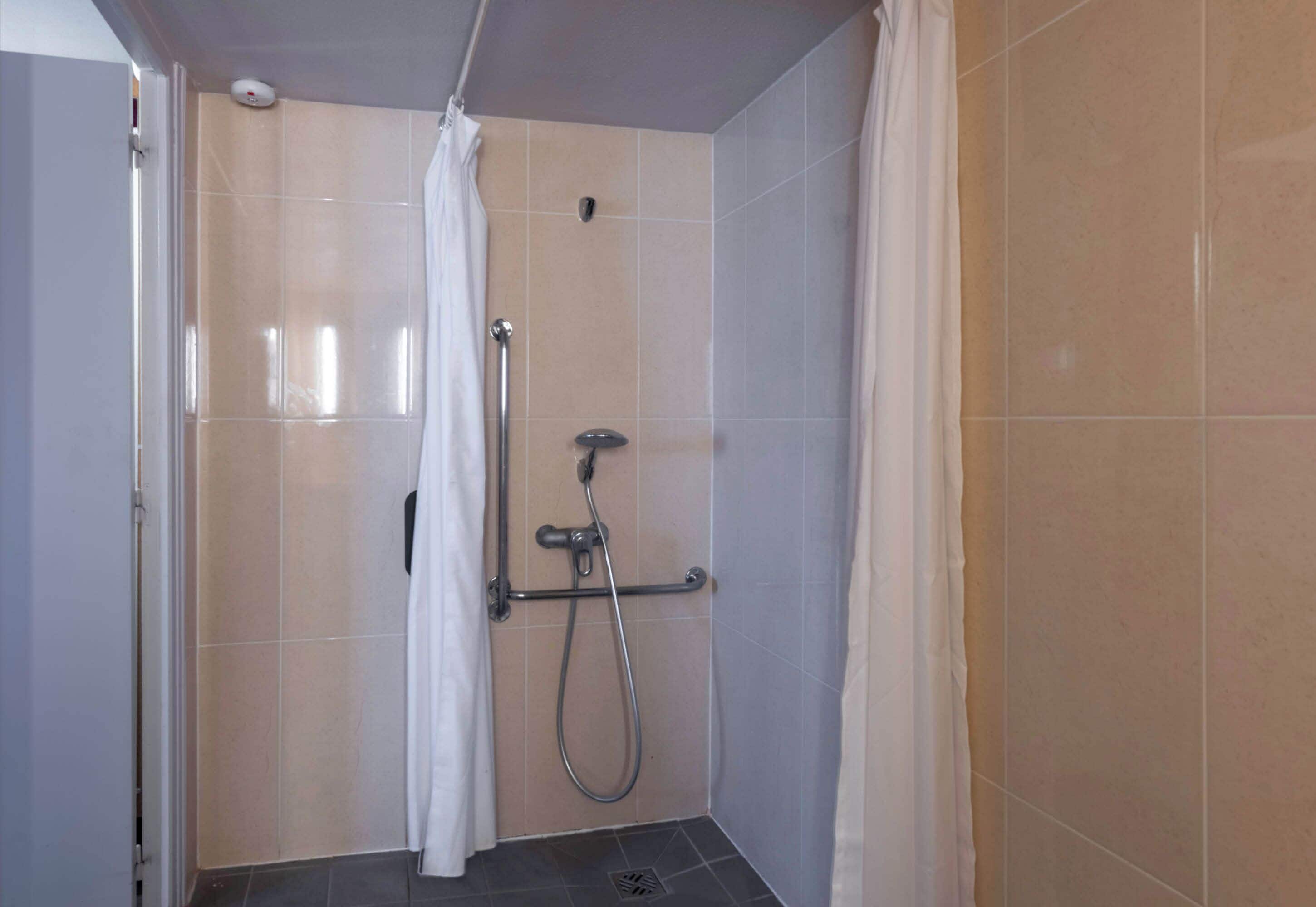 Un petit espace de douche carrelé, équipé d’un pommeau de douche à main et d’un robinet fixé au mur.
