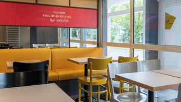 A modern restaurant interior with yellow seating, white tables, and large windows offering a view of the outdoors.