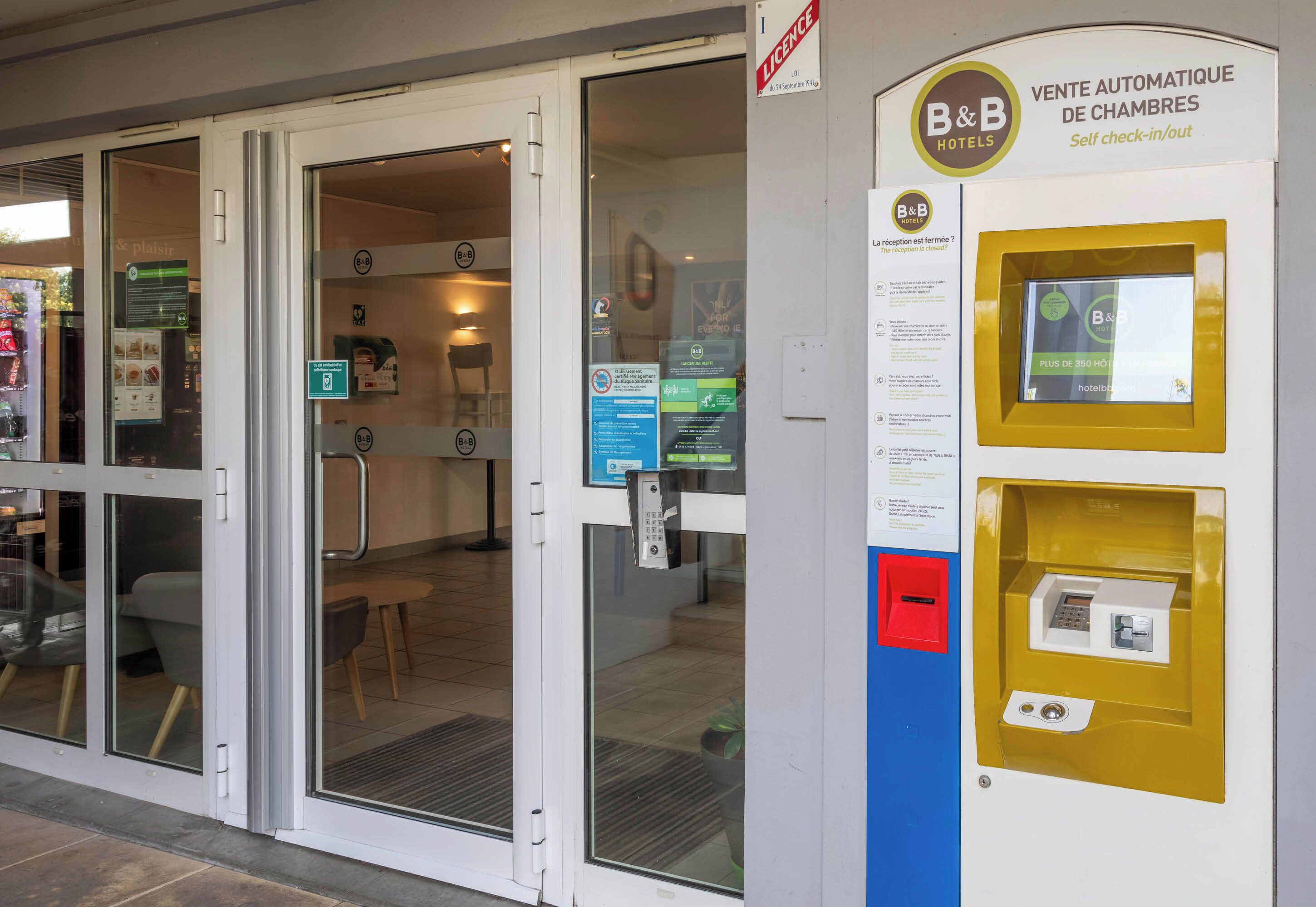 Entrada de hotel con máquinas para reservar habitaciones automáticamente y una zona de recepción.