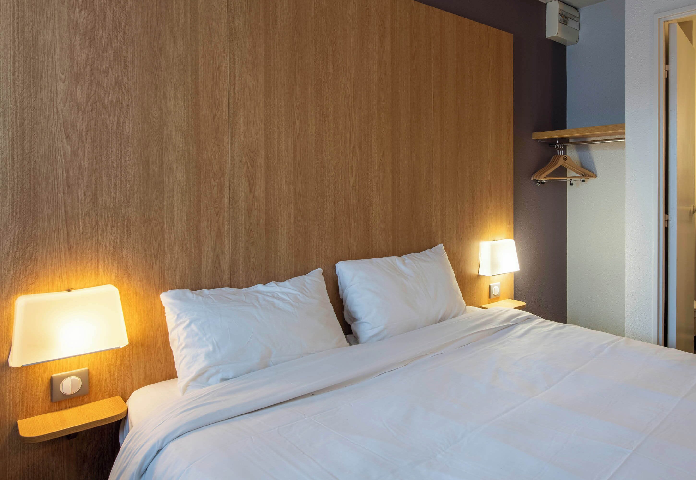 A neatly made bed with white linens and two bedside lamps.