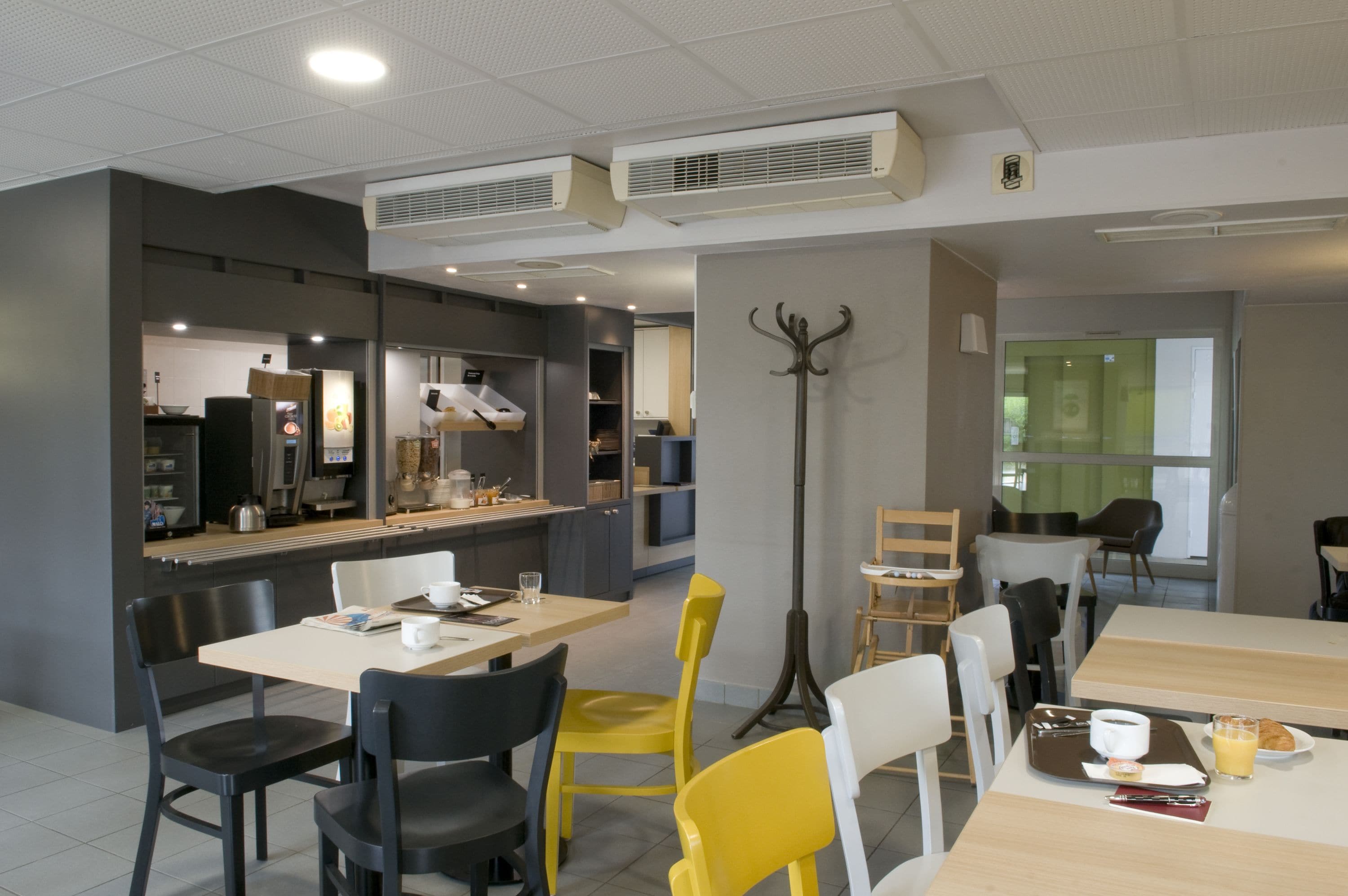 A modern dining area with tables and chairs, a coffee machine, and a counter with a menu.