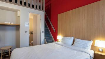 A hotel room with a bed, a nightstand, a lamp, a wooden headboard, a staircase, and a small table.