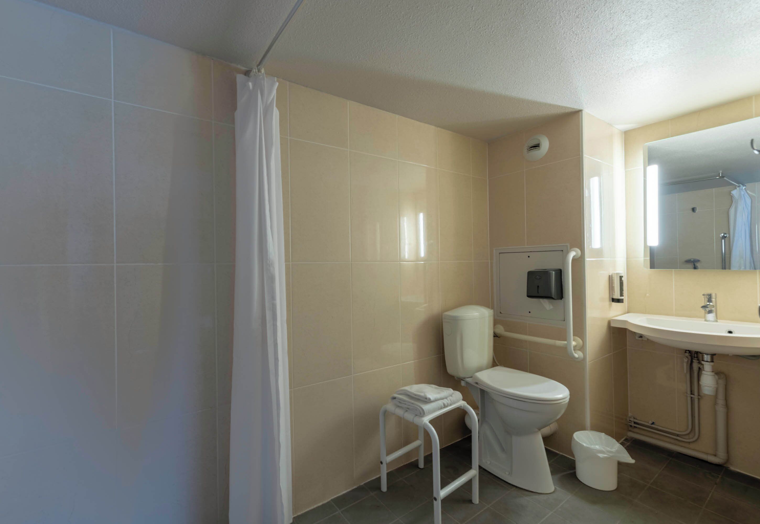 Une salle de bain comprenant des toilettes, un lavabo, une douche et un petit tabouret.