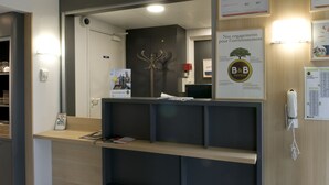 Un mostrador de recepción con un espejo, el letrero de B&B Hotels y un cartel enmarcado.