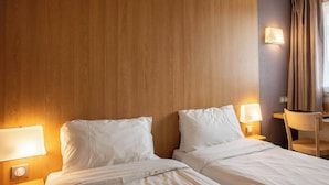 Habitación de hotel con dos camas, lámparas de noche, cabecera de madera, un escritorio y una silla.