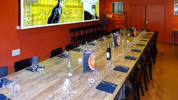 Une salle de conférence avec une longue table préparée pour une réunion, un grand écran diffusant une bande dessinée et un panneau affichant le menu des pizzas.