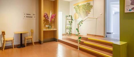 Zona de recepción con escritorio de madera, dos sillas, un mapa en la pared y una escalera con escalones amarillos.